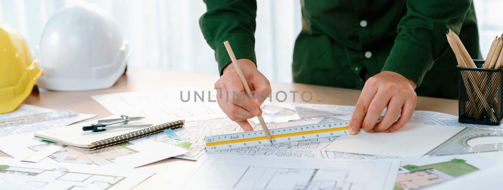 Professional engineer measuring the blueprint. Professional engineer working architectural project at studio on a table with yellow helmet and architectural equipment scatter around. Delineation.