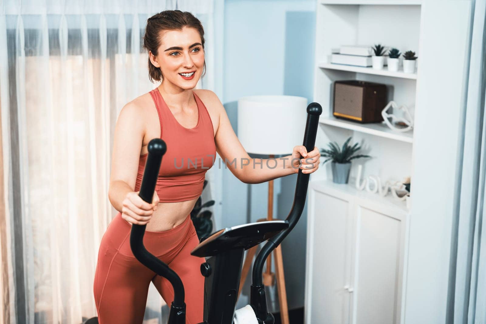 Athletic and sporty woman running on elliptical running machine at gaiety home. by biancoblue