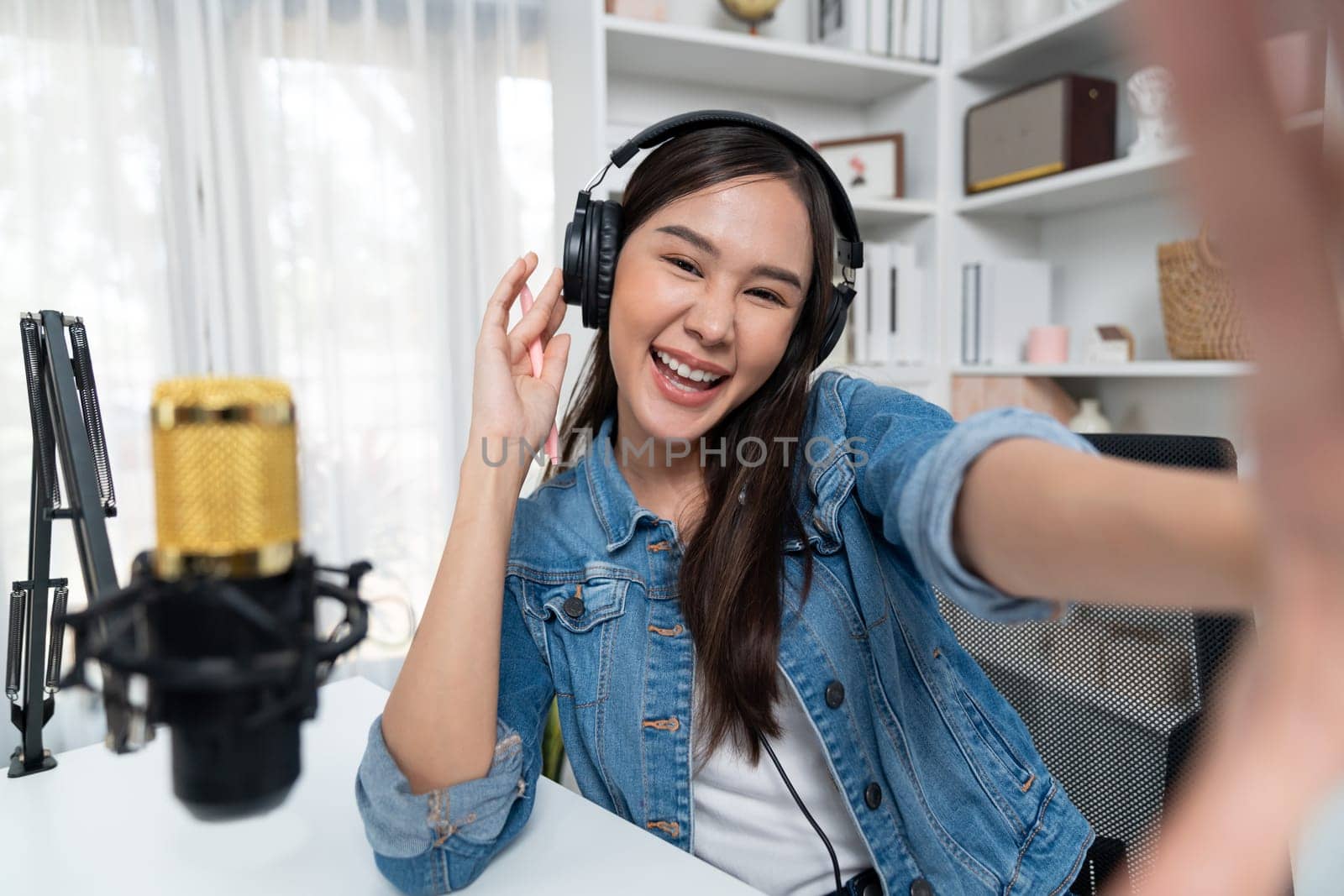 Host channel young beautiful Asian girl making selfie with smartphone wearing headphones at modern studio home office concept of behind the scene broadcaster live streaming on social media. Stratagem.
