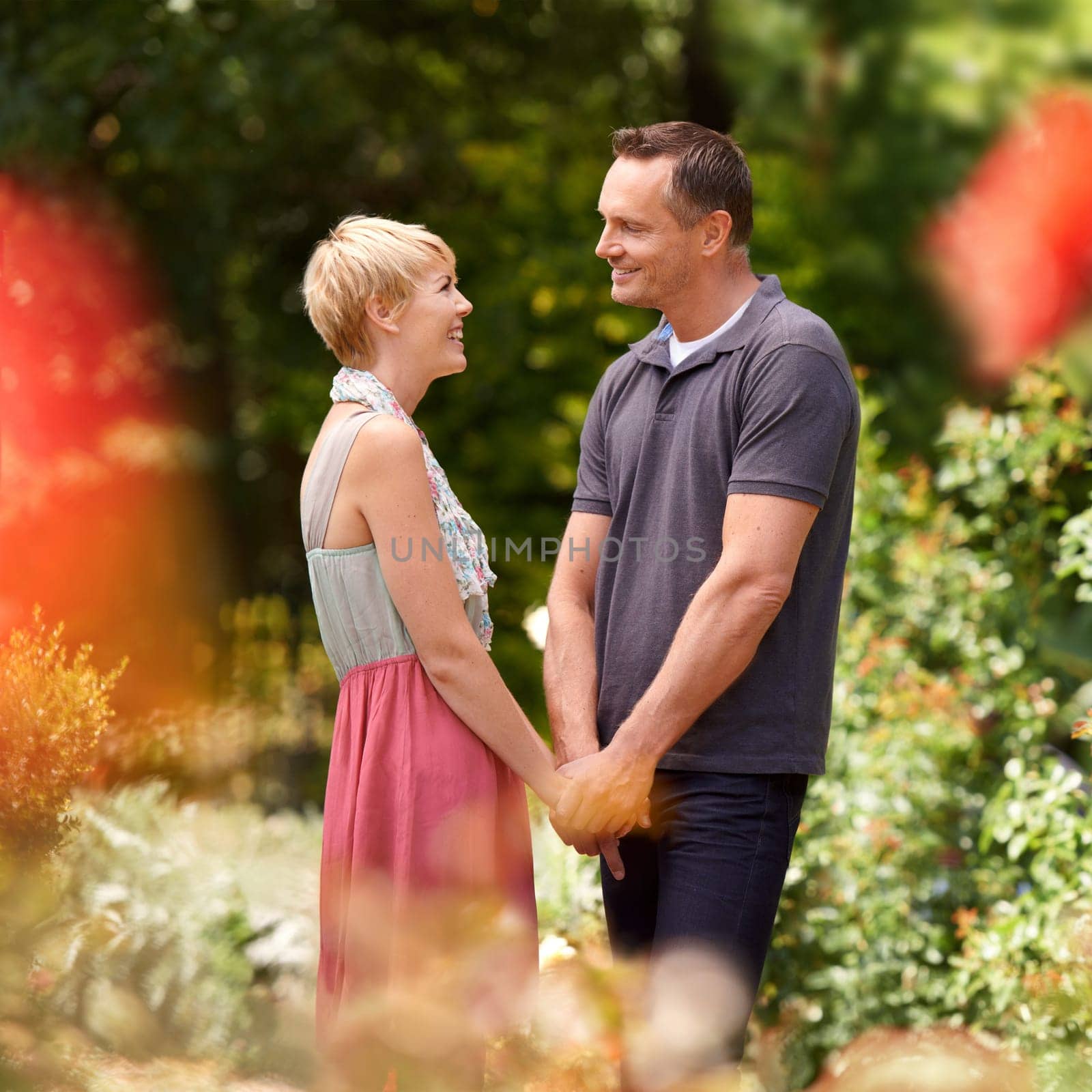 Happy, holding hands and couple in a park with love, trust and support, solidarity and security while bonding in nature. Commitment, care and people on a field of flowers for spring romance or date.