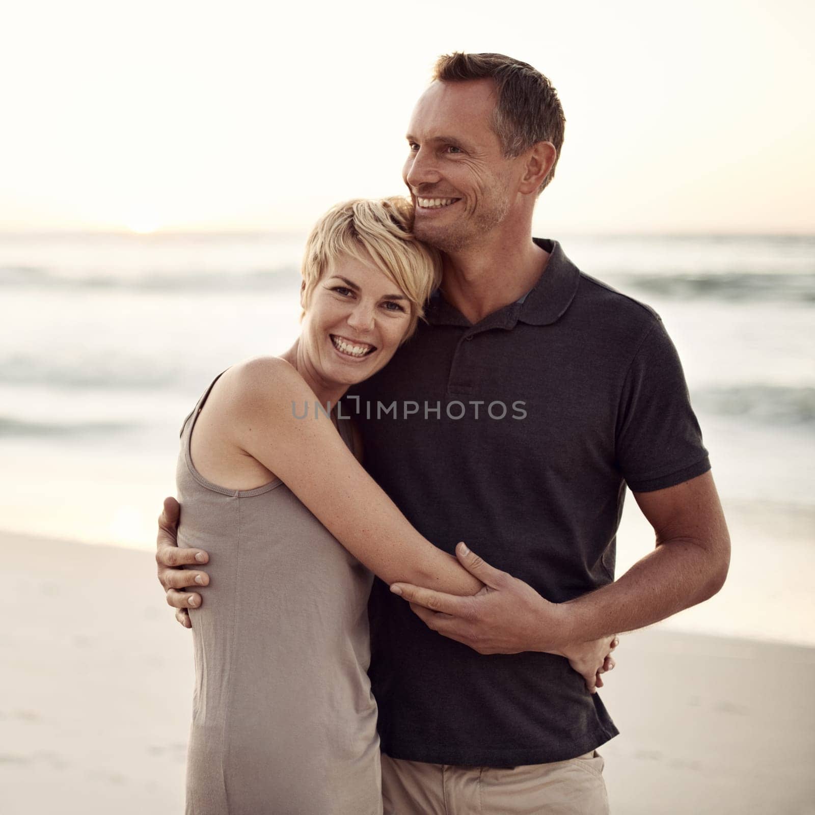 Couple, portrait and happy on beach with hug for bonding, honeymoon date and weekend holiday in California. Face, man and woman with embrace, smile and love by sea for vacation, travel and adventure.