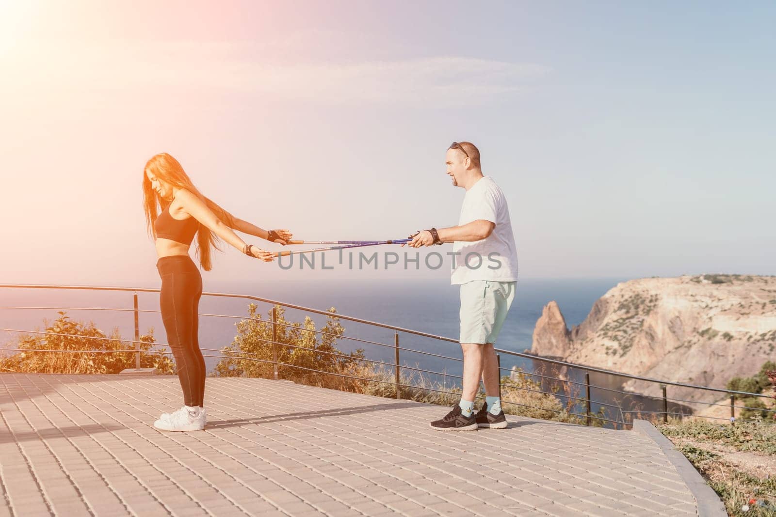 Happy Middle aged couple or friends practicing nordic walking in park near sea. Mature couple with trekking poles walking, practicing Nordic walking outdoors. Aging youthfully and sport concept.