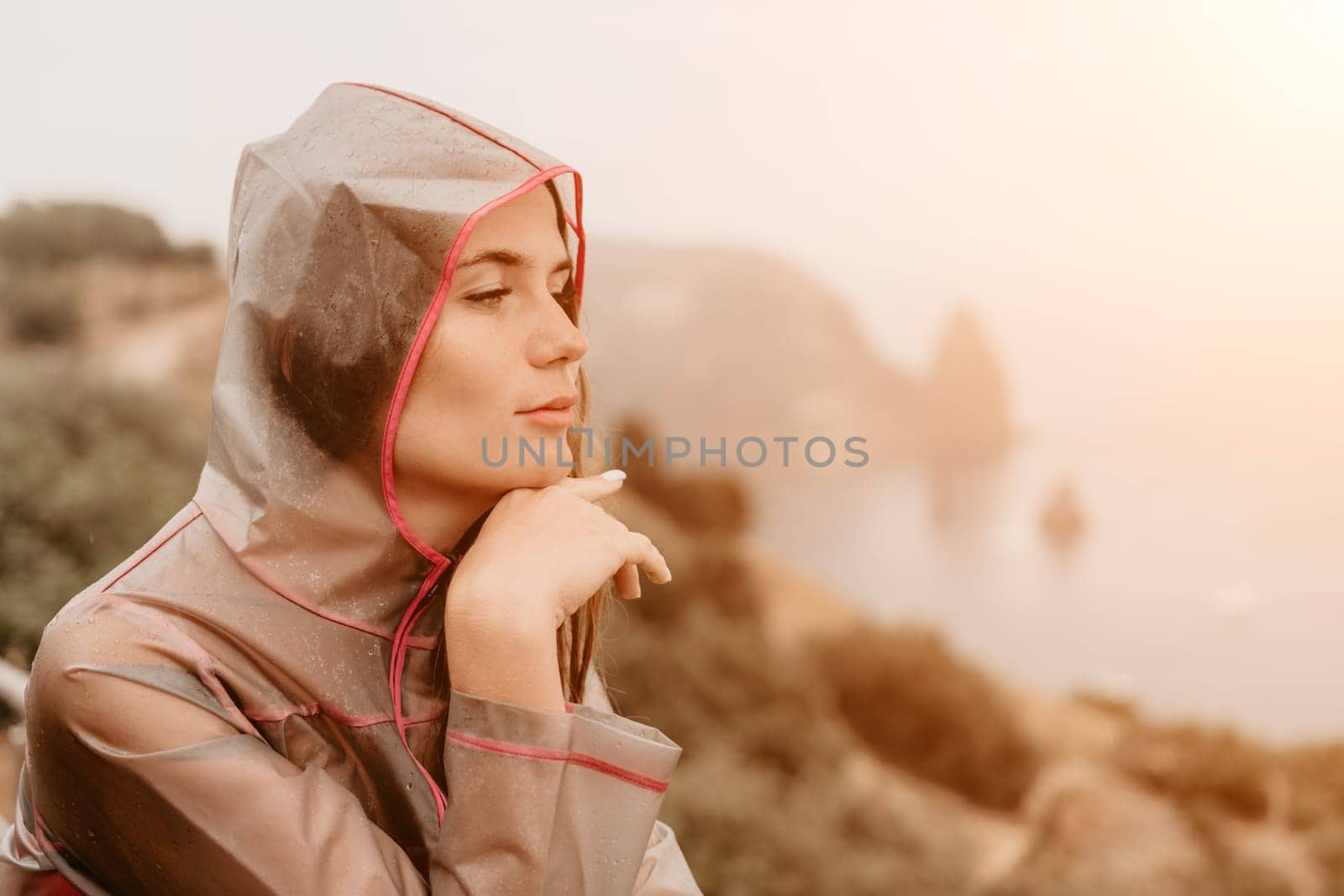 Woman rain umbrella. Happy woman portrait wearing a raincoat with transparent umbrella outdoors on rainy day in park near sea. Girl on the nature on rainy overcast day. by panophotograph