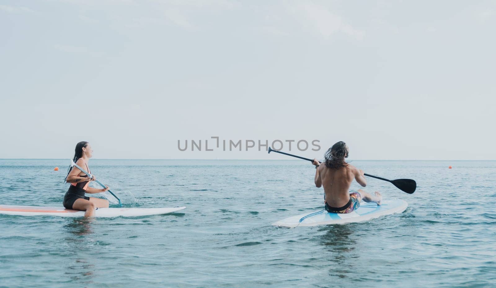 Woman man sup yoga. Happy young sporty couple practising yoga pilates on paddle sup surfboard. Female stretching doing workout on sea water. Modern family outdoor summer sport activity. by panophotograph