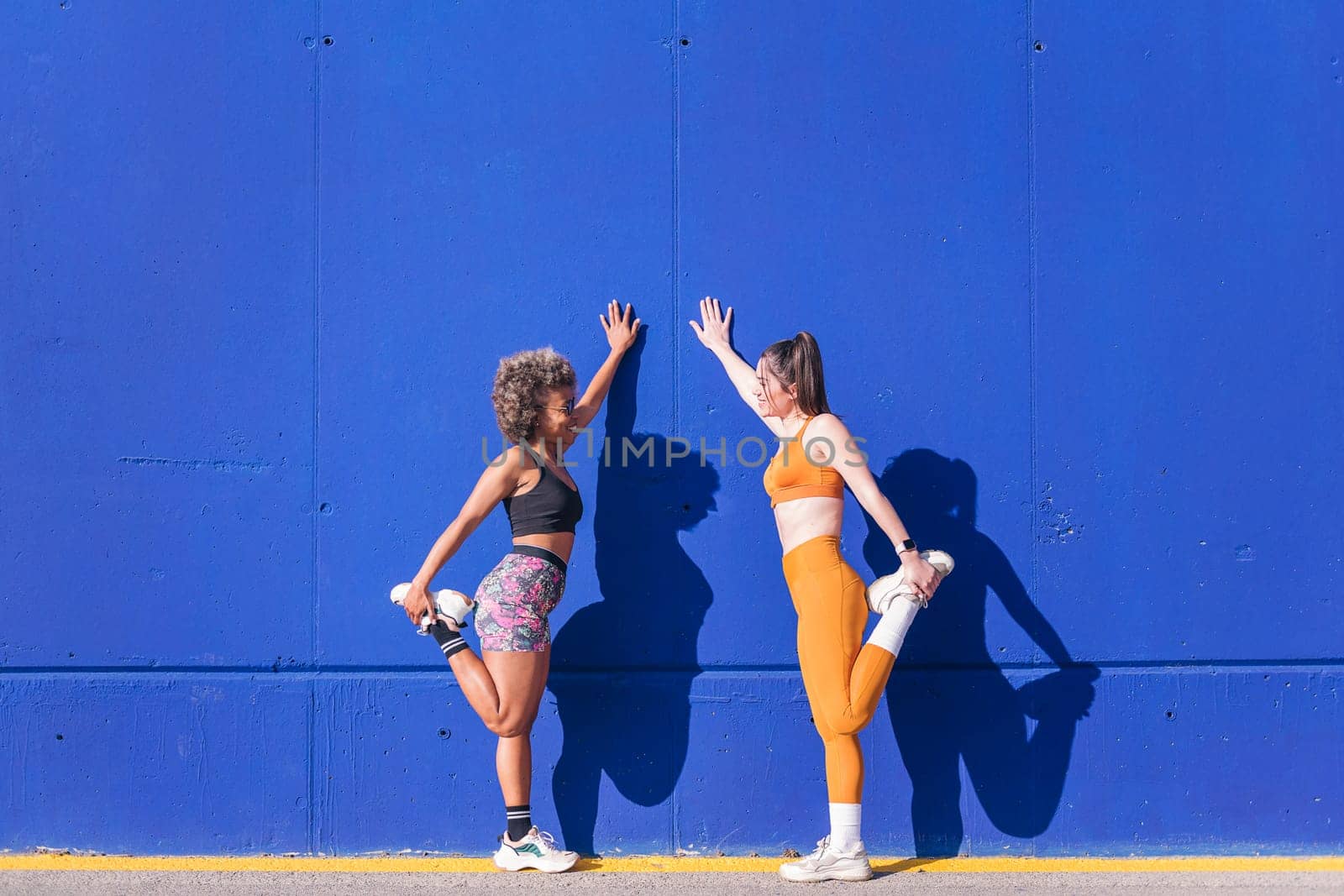 two sportswomen stretching together outdoors in a sunny day, concept of friendship in sport and active lifestyle, copy space for text