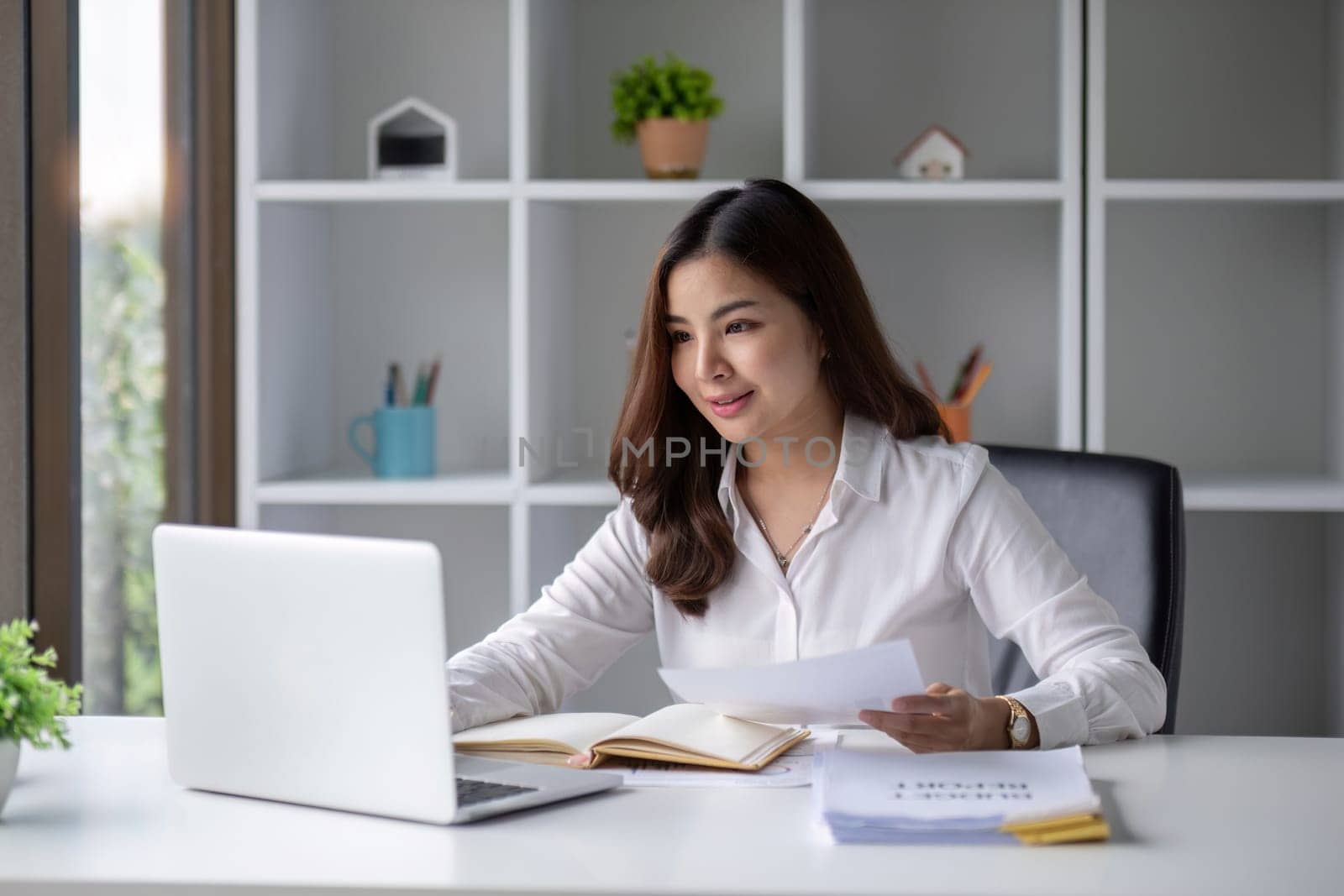 Young beautiful business woman using laptop and checking documents while working on laptop by wichayada