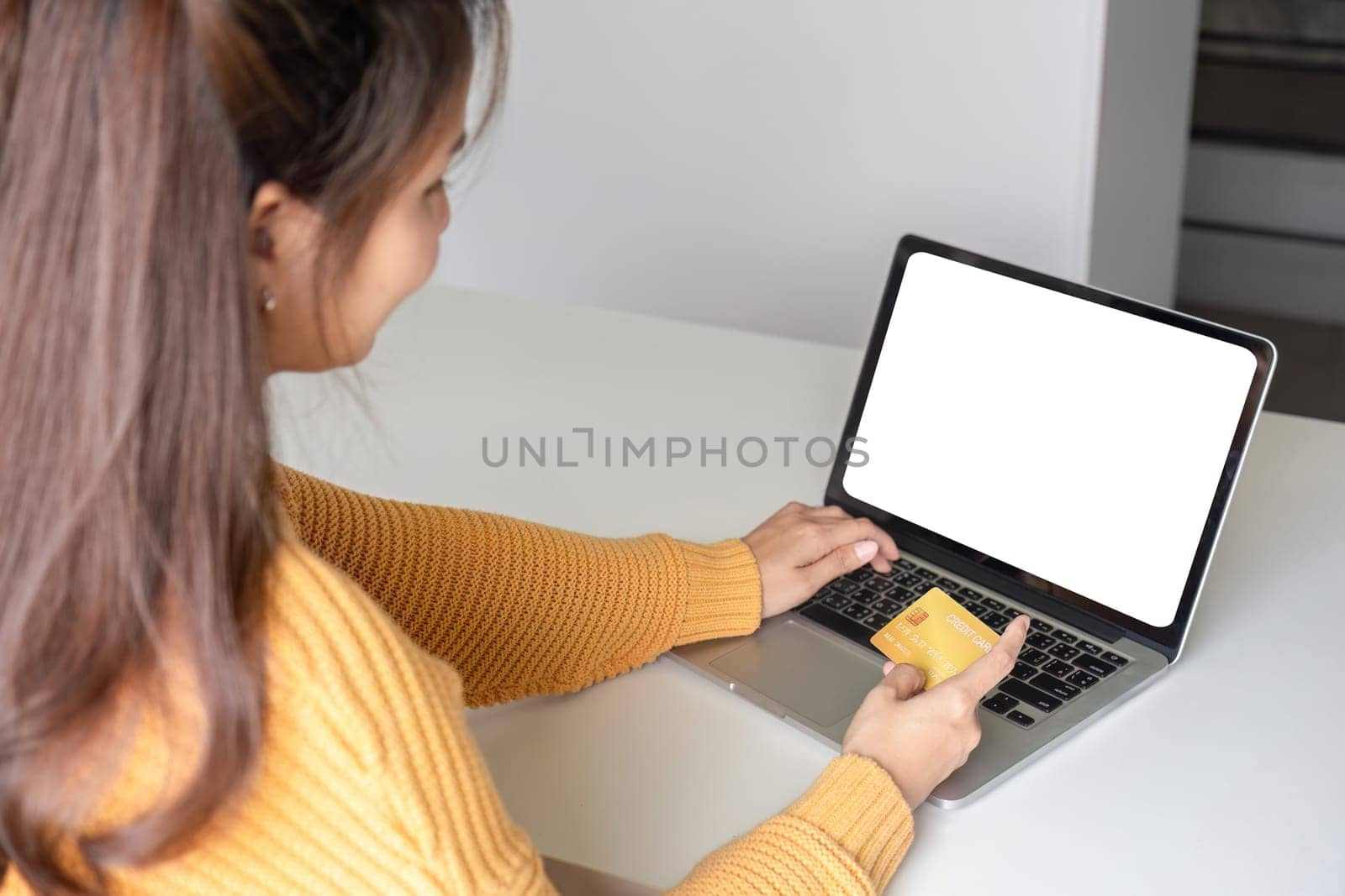 Young Asian woman uses credit card to shop online on laptop.