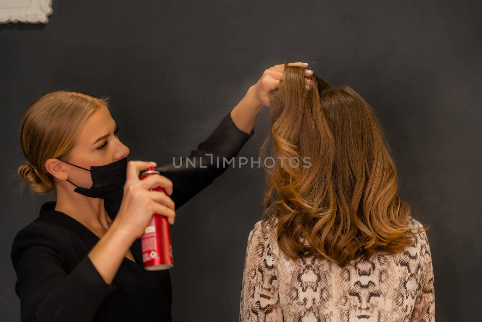 Women salon hairstyle. Hairdresser uses hairspray on client's hair in salon, Portrait of two beautiful women.