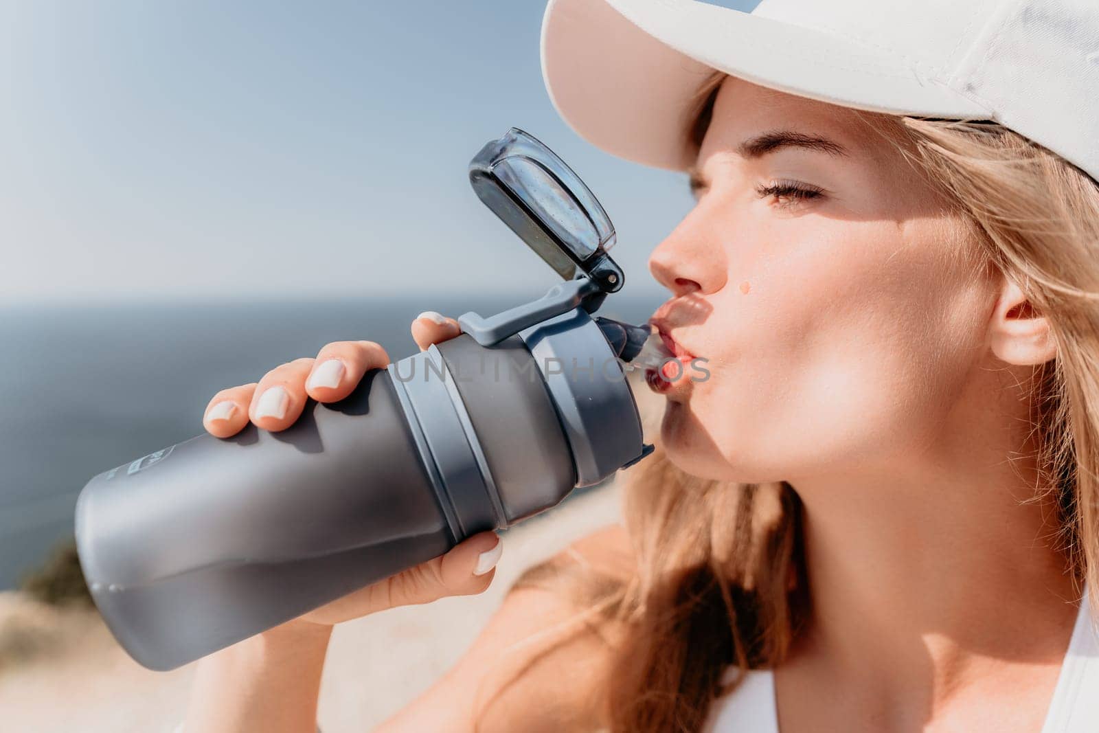 Fintess woman drinking water. Happy, active middle aged woman standing on beach and drinking water after excersise. Concept of lifestyle, sport. Close up by panophotograph