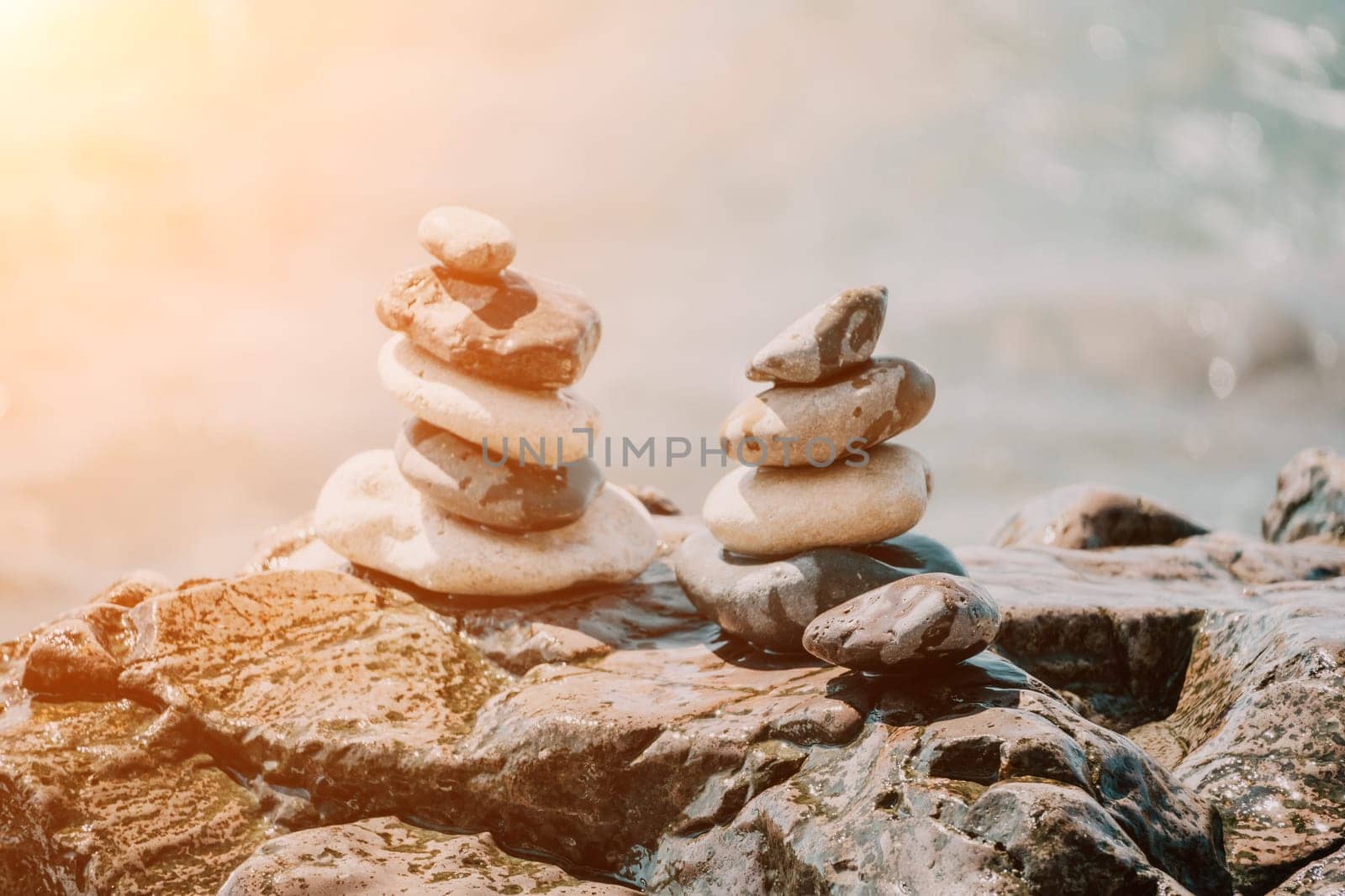 Balanced rock pyramid on pebbles beach, sunny day and clear sky at sunset. Golden sea bokeh on background. Selective focus, zen stones on sea beach, meditation, spa, harmony, calm, balance concept. by panophotograph