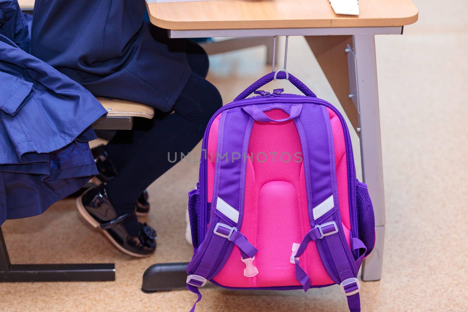 The school backpack hangs on a hook at the desk where the student sits. by Yurich32
