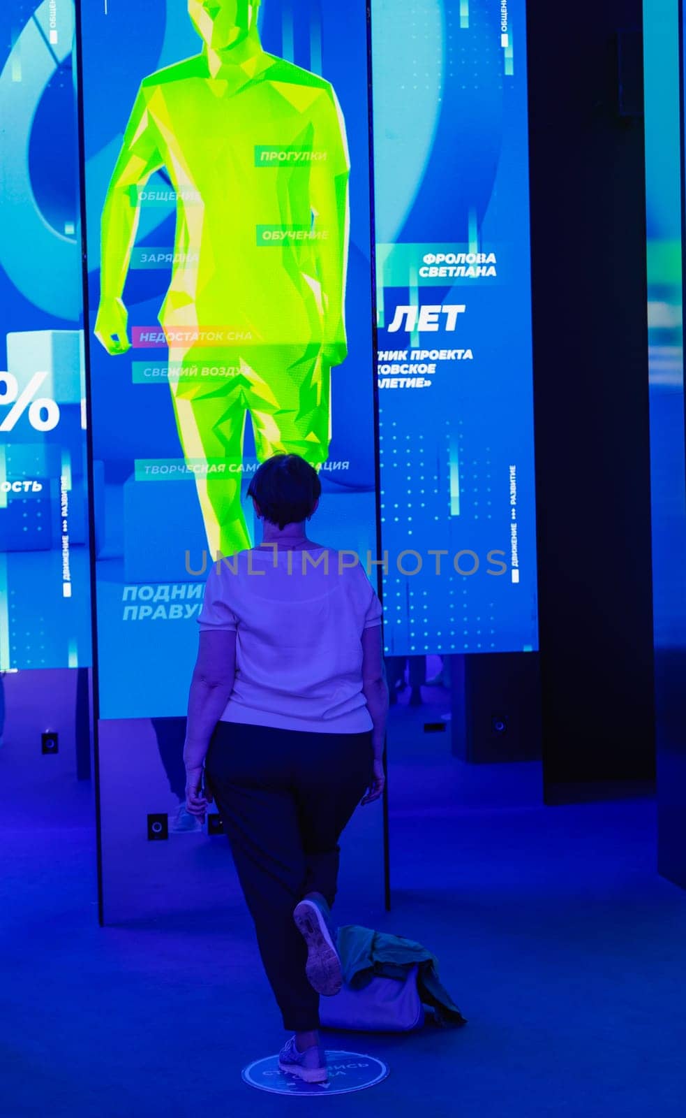 A woman performs exercises while looking at a huge monitor. Futuristic forum in Moscow. Moscow, Russia, August 19, 2023. by Yurich32