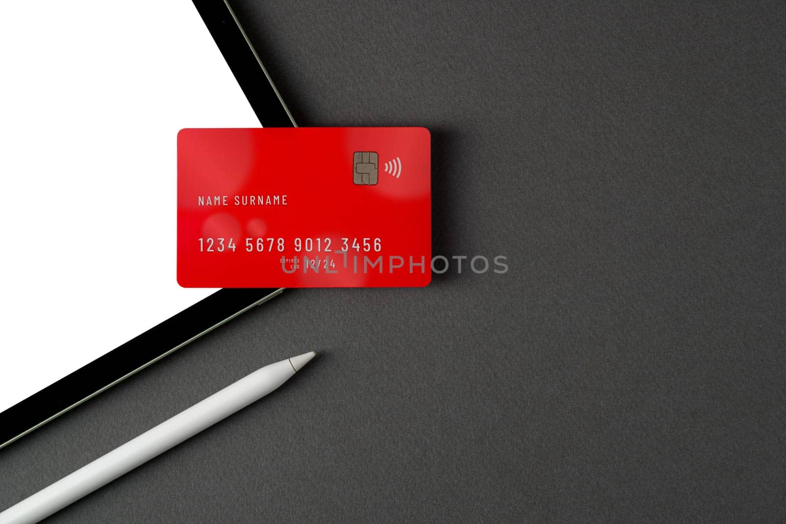 Credit card lying on tablet with blank screen on dark gray table by Sonat