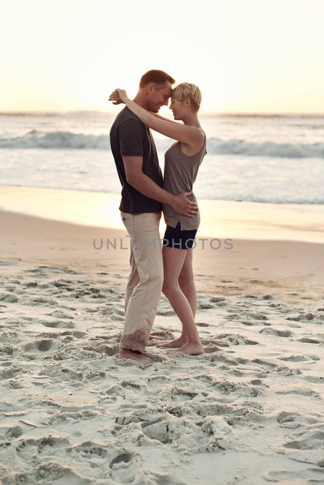Couple, together and beach with sunset for romance with peace in trip and vacation. Partners, embrace and relax in sea to enjoy, calm and smile for love of marriage in honeymoon and holiday.