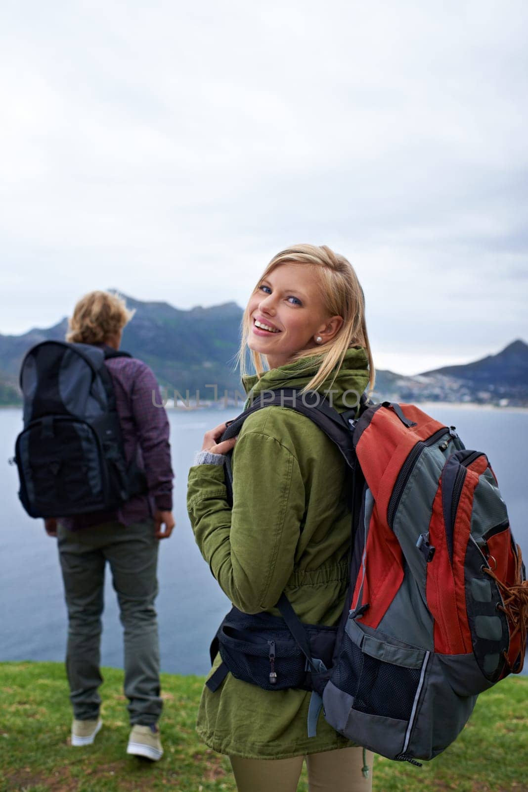Happy couple, portrait and hiking with backpack for adventure, travel or outdoor journey together in nature. Young man and woman with smile and bag for trekking, explore or fitness by the ocean coast by YuriArcurs
