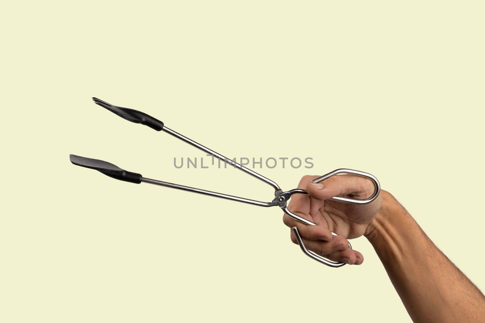 Male hand holding kitchen tong isolated on light green background. High quality photo