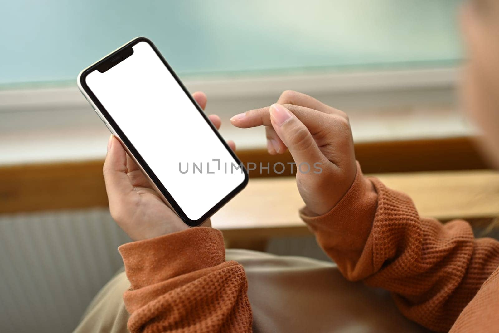 Woman in sweater using mobile phone while sitting on sofa. Empty screen for advertising text message by prathanchorruangsak