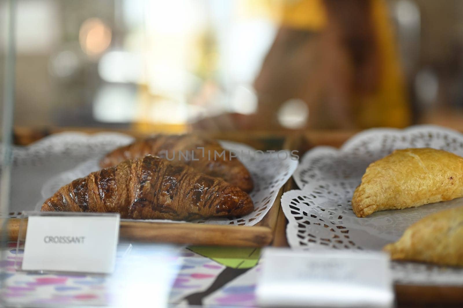 Freshly baked chocolate croissants and pies in glass showcase at bakery.