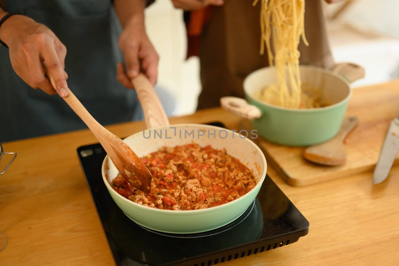 Closeup young couple cooking bolognese spaghetti sauce for dinner in a frying pan.