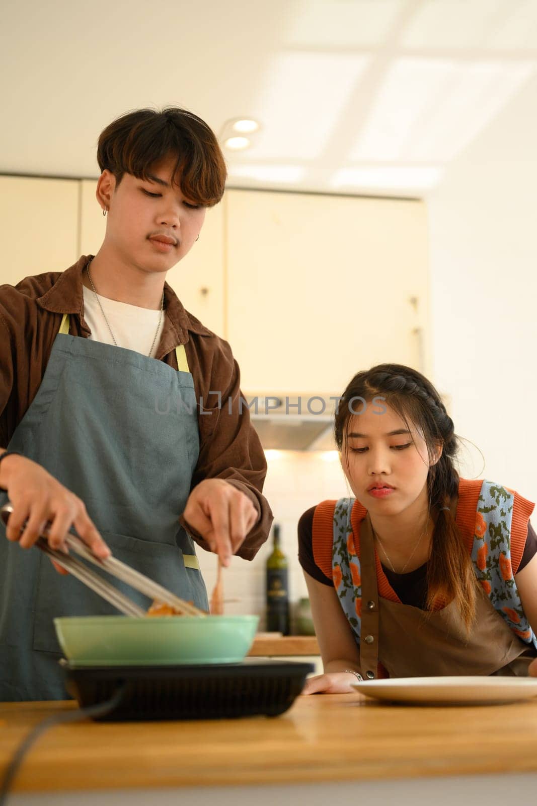 Portrait of Asian couple wearing aprons cooking together in the kitchen at home by prathanchorruangsak