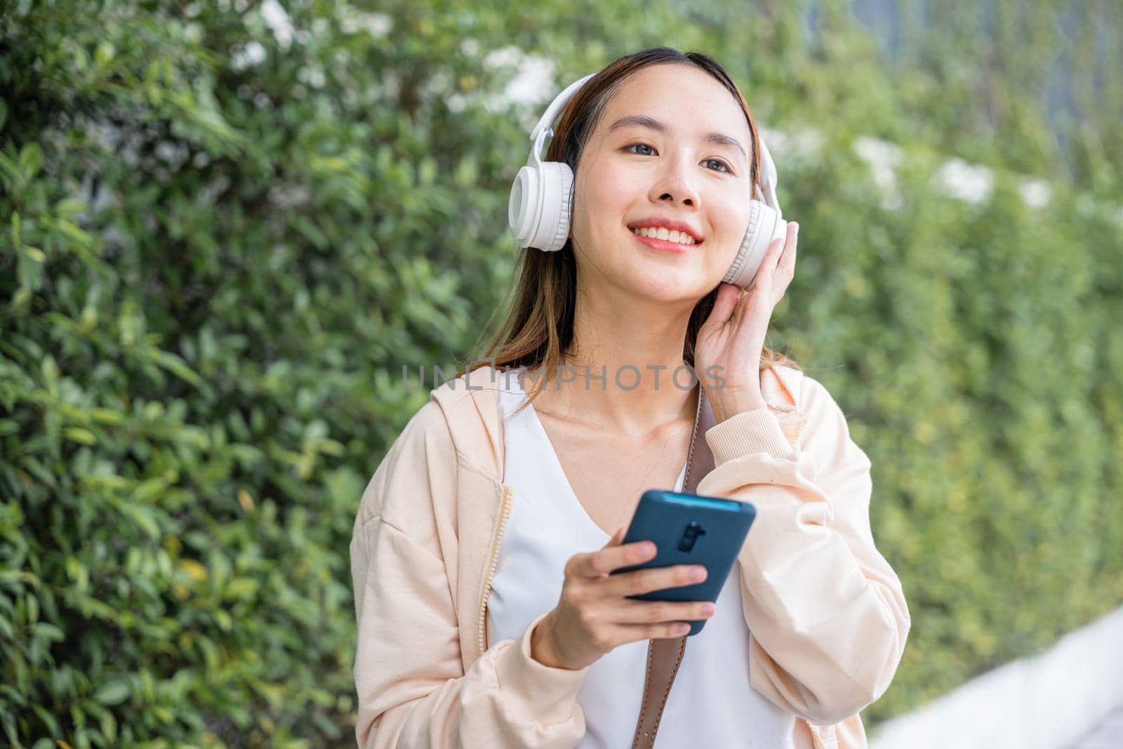 A cheerful young woman dancing with wireless headphones immerses herself in joy of choosing and listening to her favorite energetic music outdoors in the urban city garden. season beauty is evident. by Sorapop