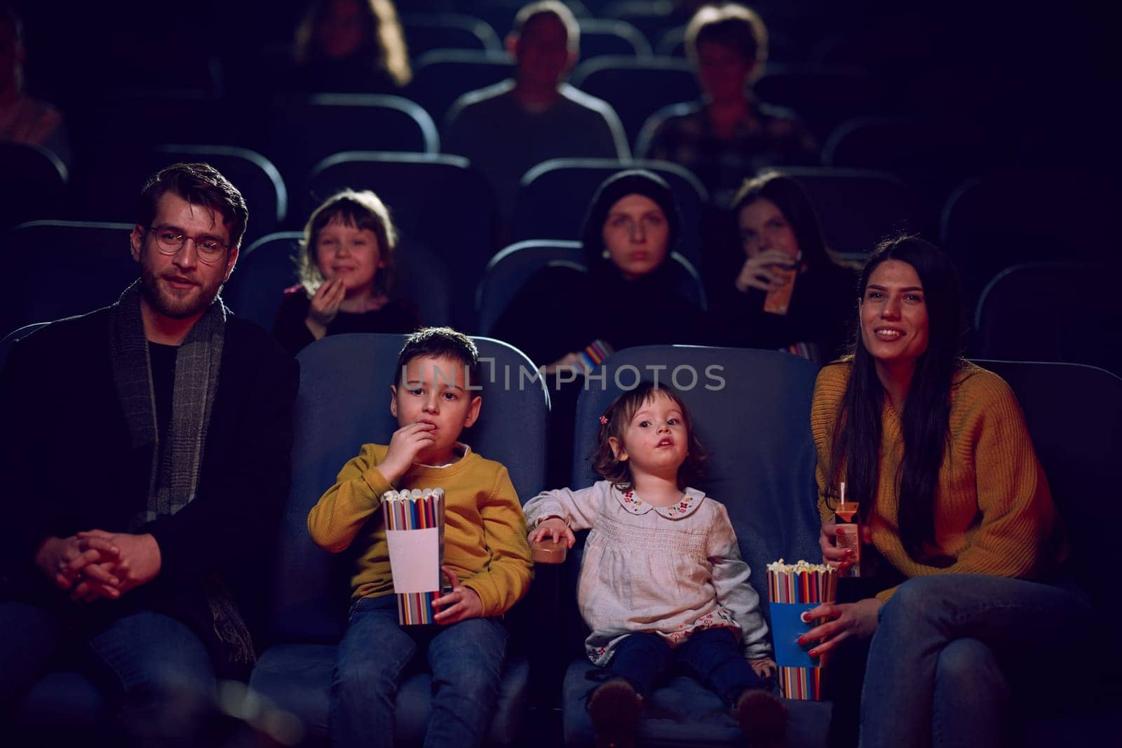 A modern family enjoys quality time together at the cinema, indulging in popcorn while watching a movie with their children.