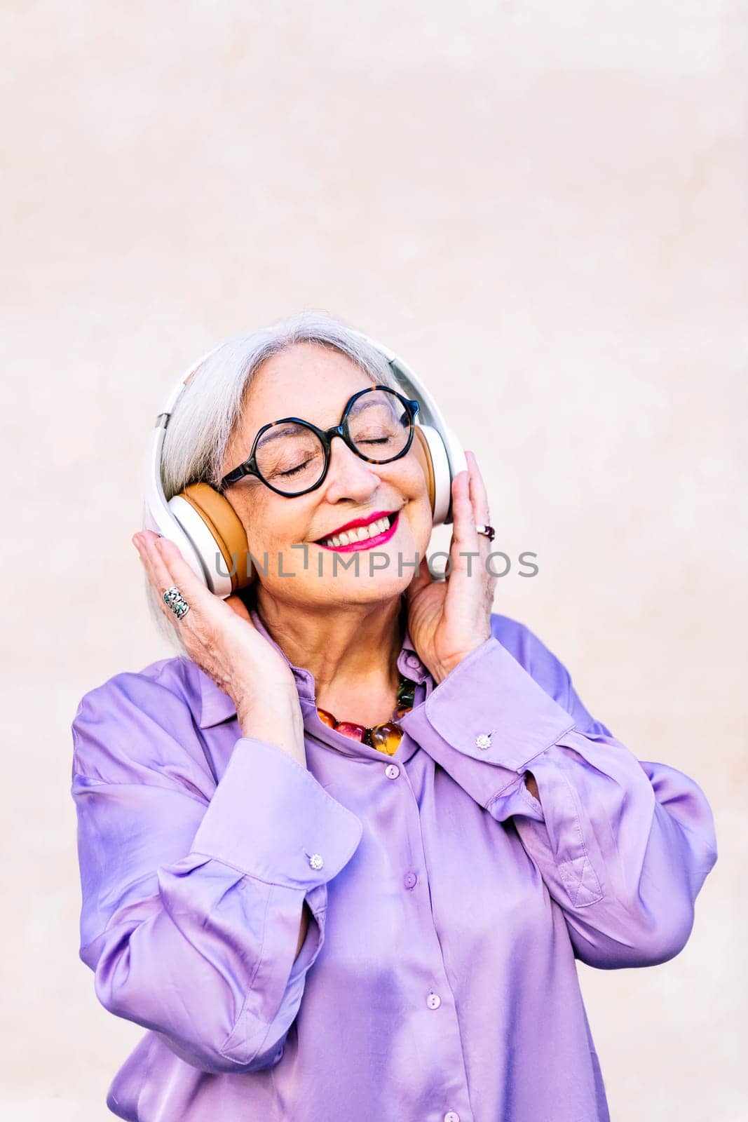 smiling senior woman in glasses enjoying music in her headphones, concept of elderly people leisure and active lifestyle, copy space for text