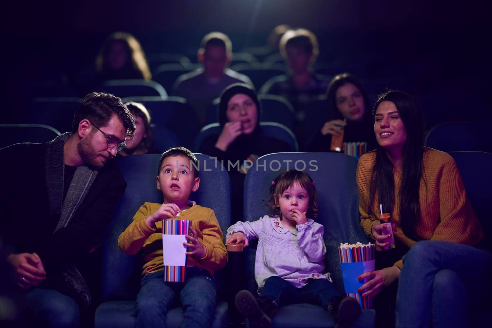 A modern family enjoys quality time together at the cinema, indulging in popcorn while watching a movie with their children.