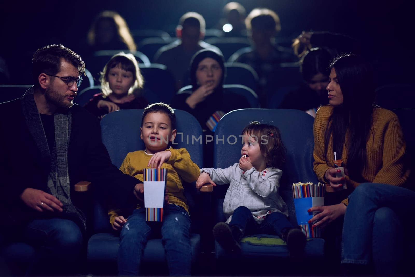 A modern family enjoys quality time together at the cinema, indulging in popcorn while watching a movie with their children by dotshock