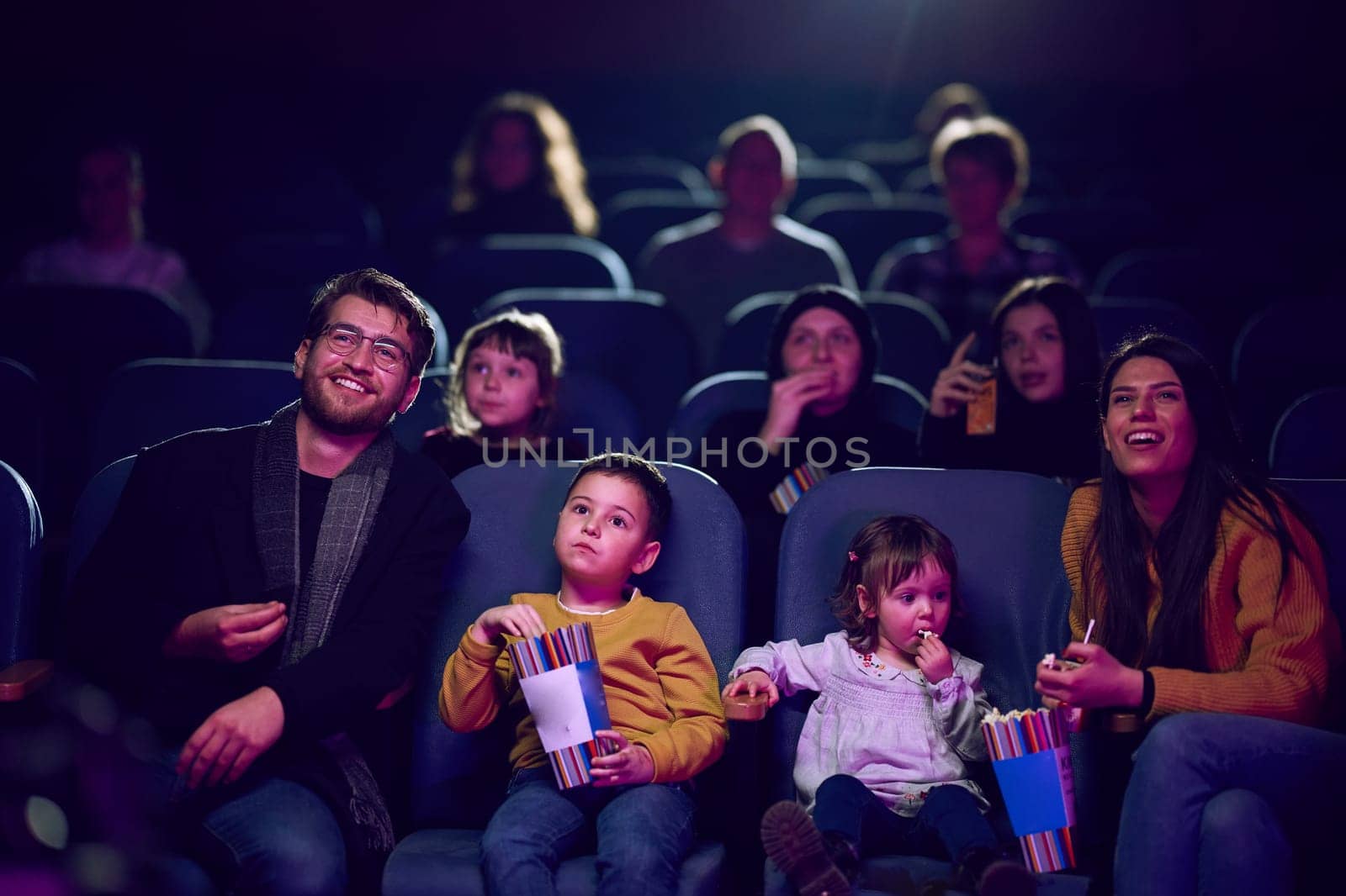 A modern family enjoys quality time together at the cinema, indulging in popcorn while watching a movie with their children.