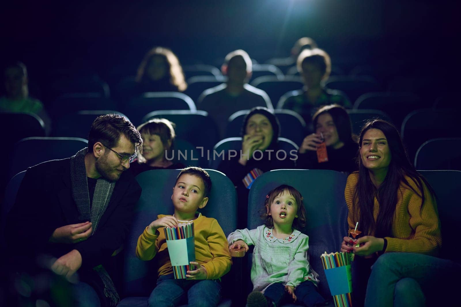 A modern family enjoys quality time together at the cinema, indulging in popcorn while watching a movie with their children.