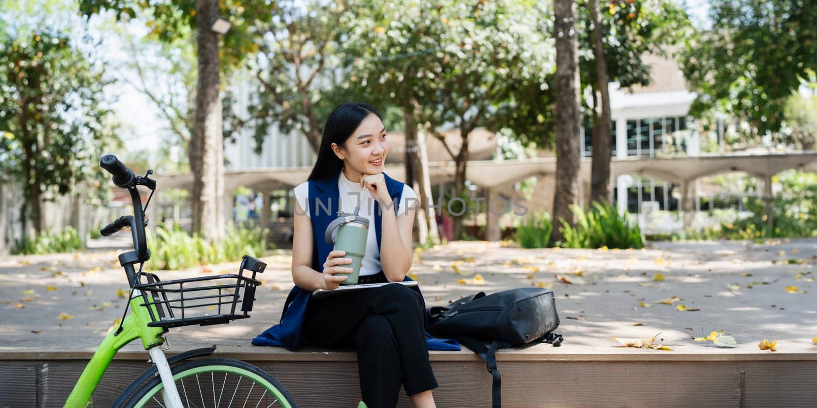 Asian young businesswoman bike to work for eco friendly green energy and hold reusable cup while commuting in city. Eco friendly by itchaznong