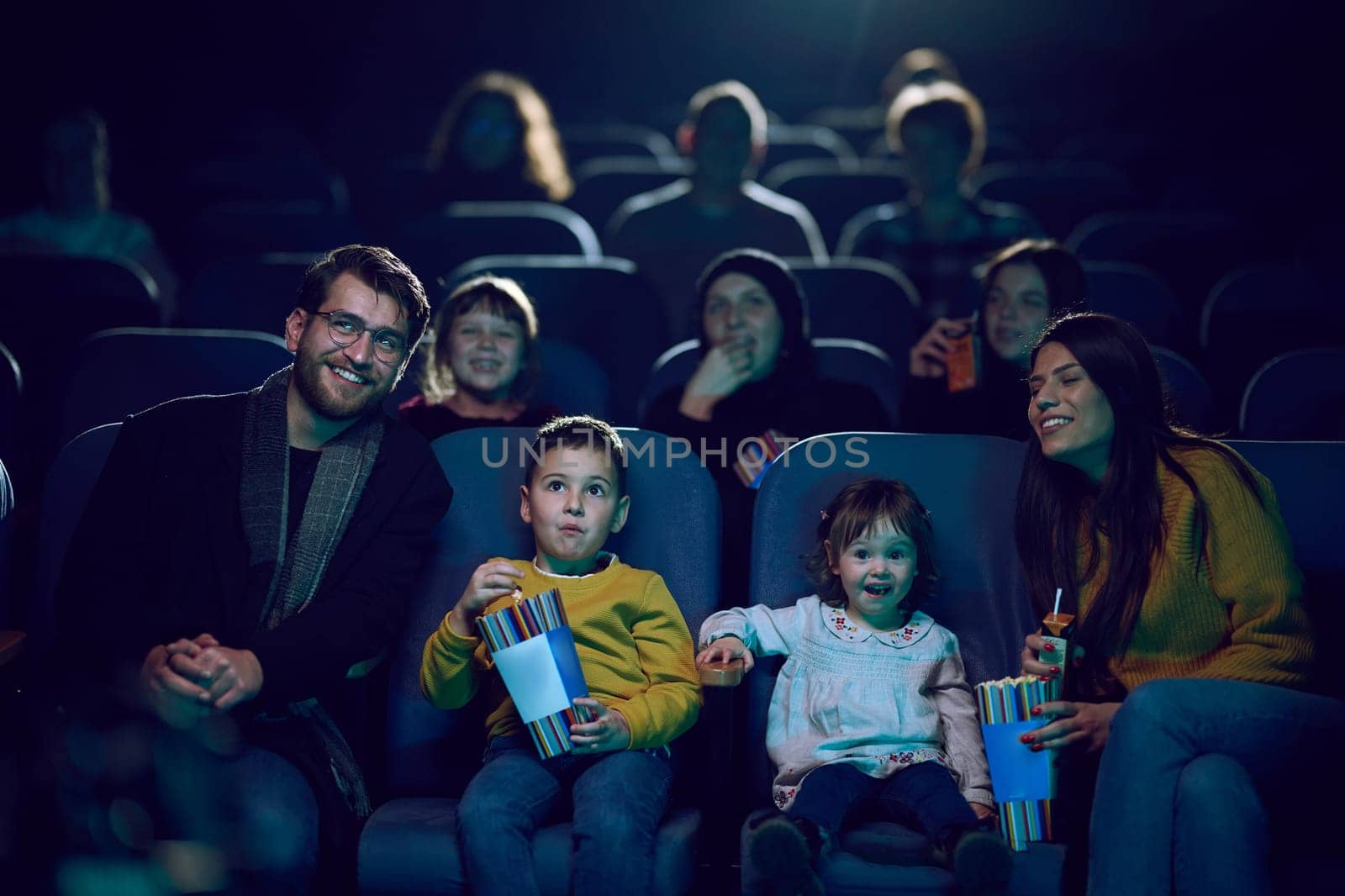 A modern family enjoys quality time together at the cinema, indulging in popcorn while watching a movie with their children by dotshock