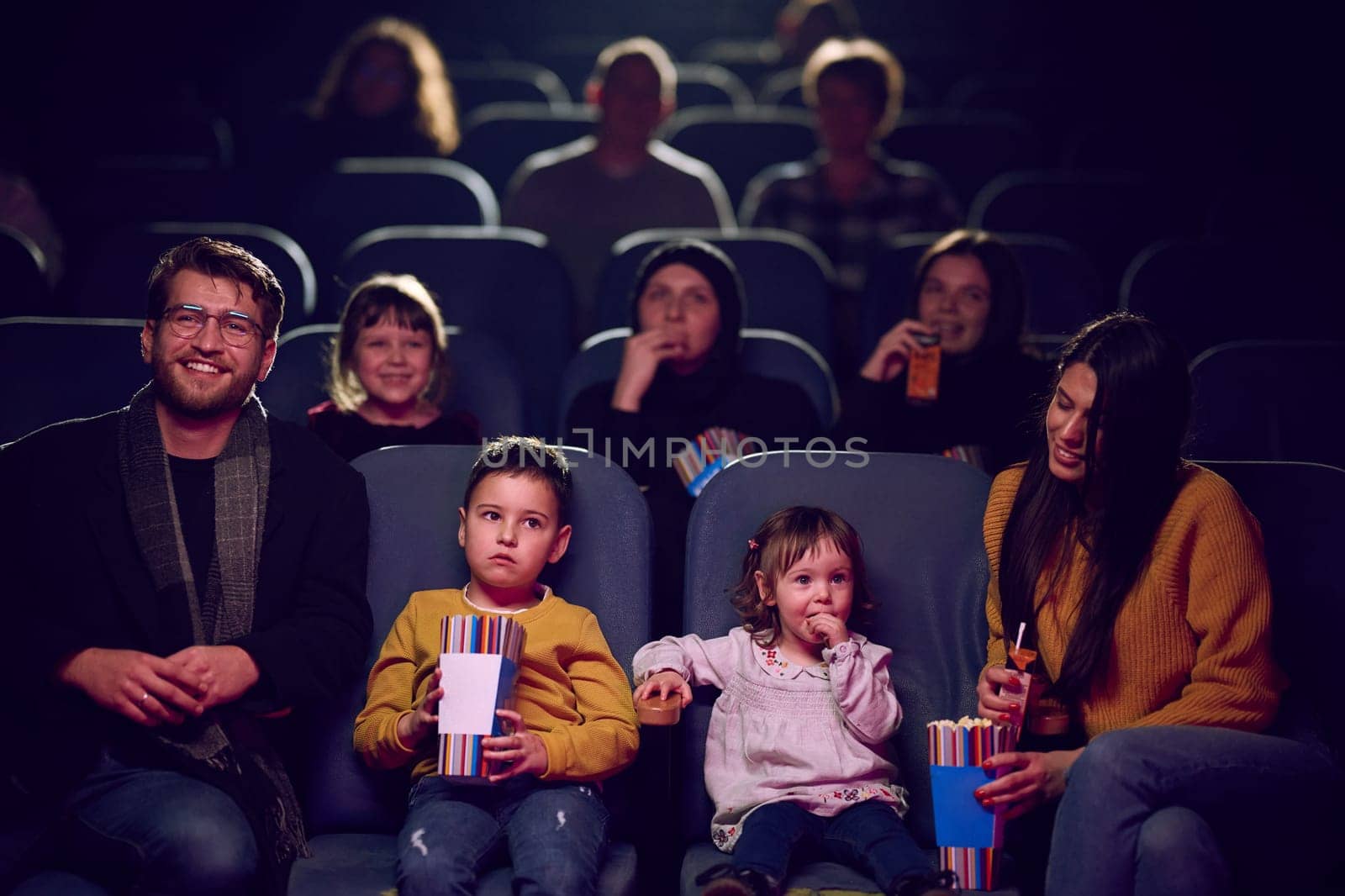 A modern family enjoys quality time together at the cinema, indulging in popcorn while watching a movie with their children.