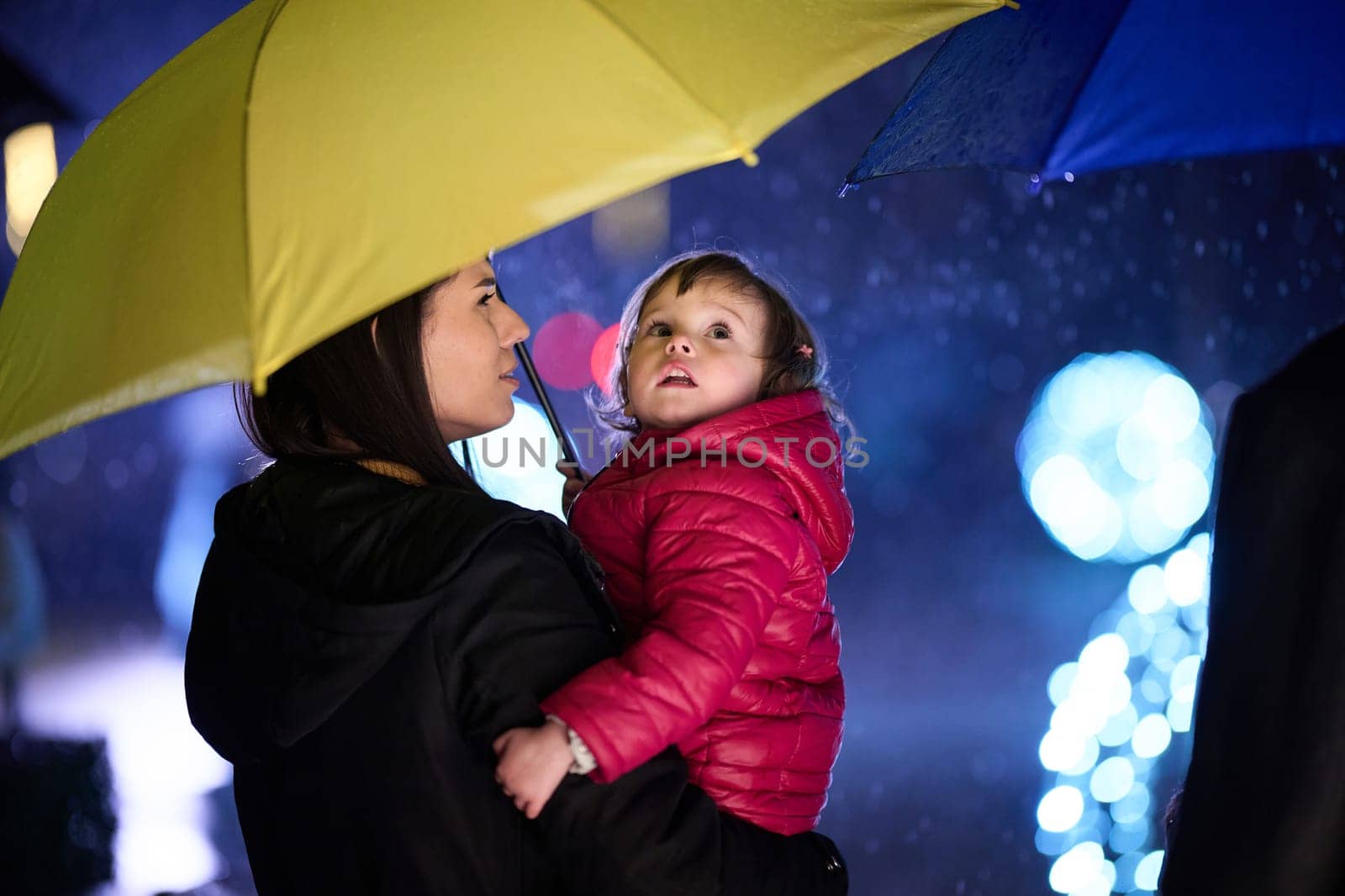 In the midst of a rainy urban night, a happy couple takes their children on a stroll through the city streets, heading towards the cinema for a delightful family movie outing.