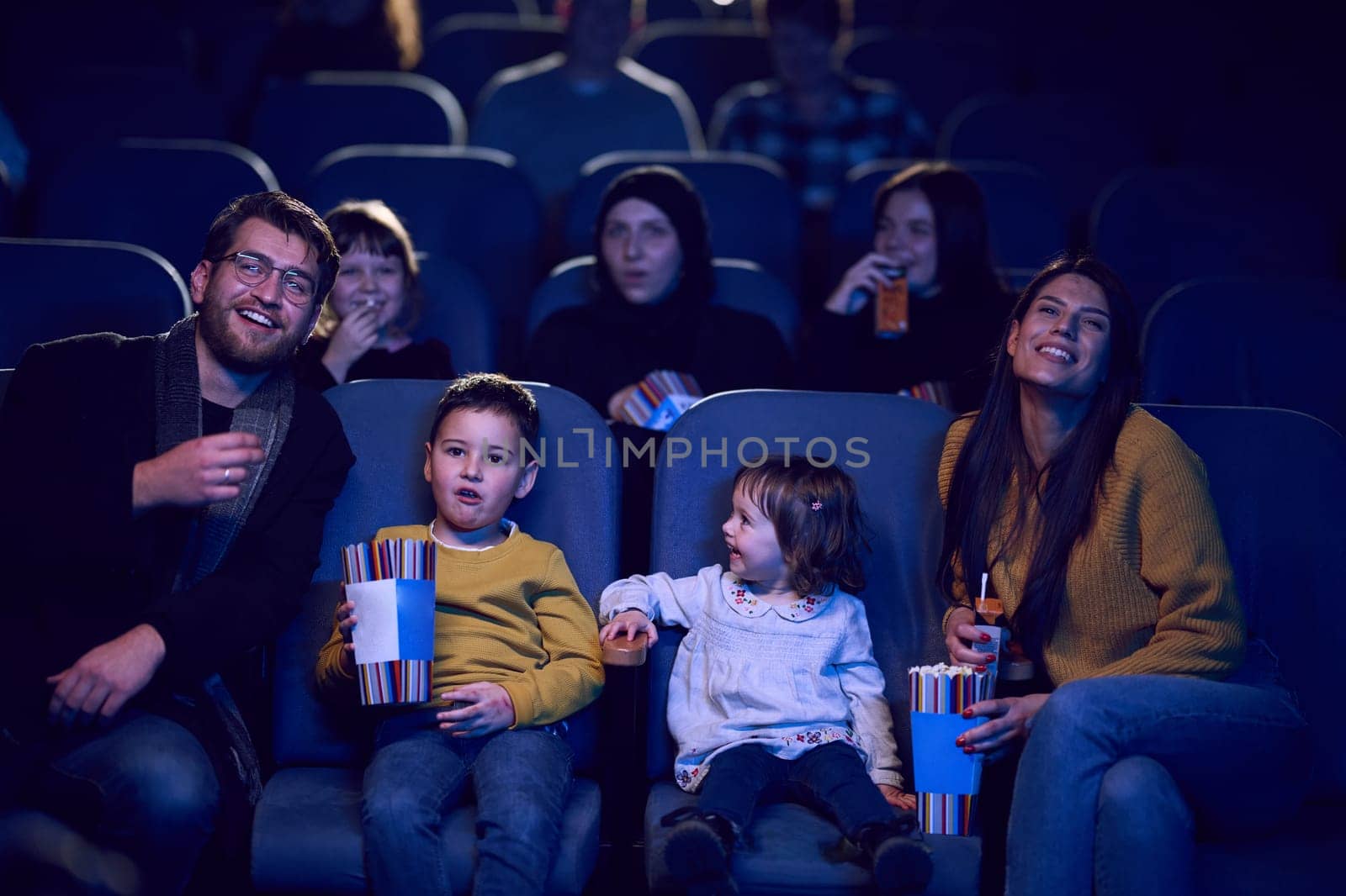 A modern family enjoys quality time together at the cinema, indulging in popcorn while watching a movie with their children.