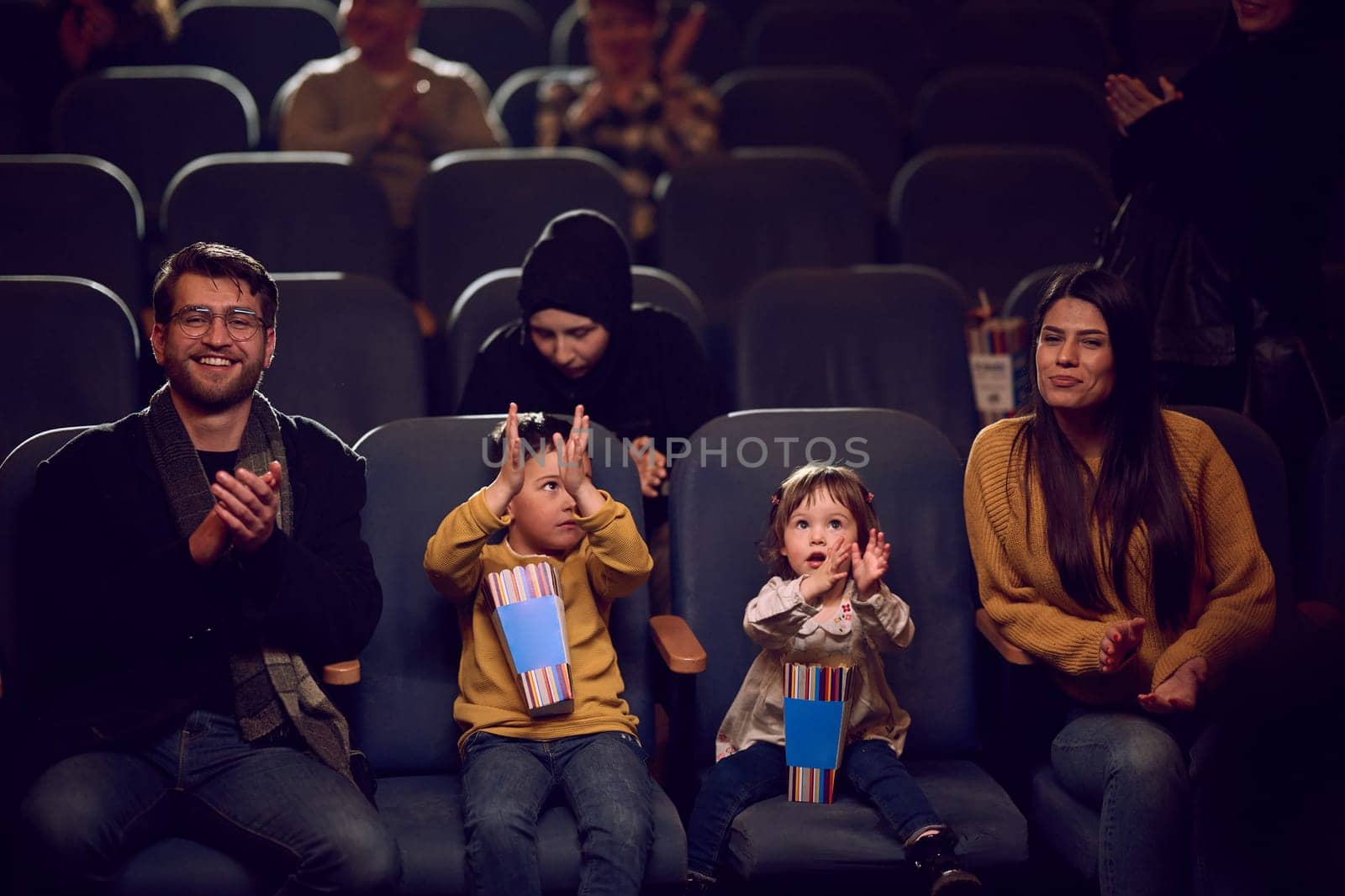 A modern family enjoys quality time together at the cinema, indulging in popcorn while watching a movie with their children.