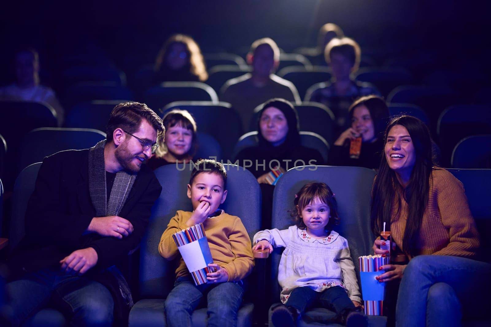 A modern family enjoys quality time together at the cinema, indulging in popcorn while watching a movie with their children.