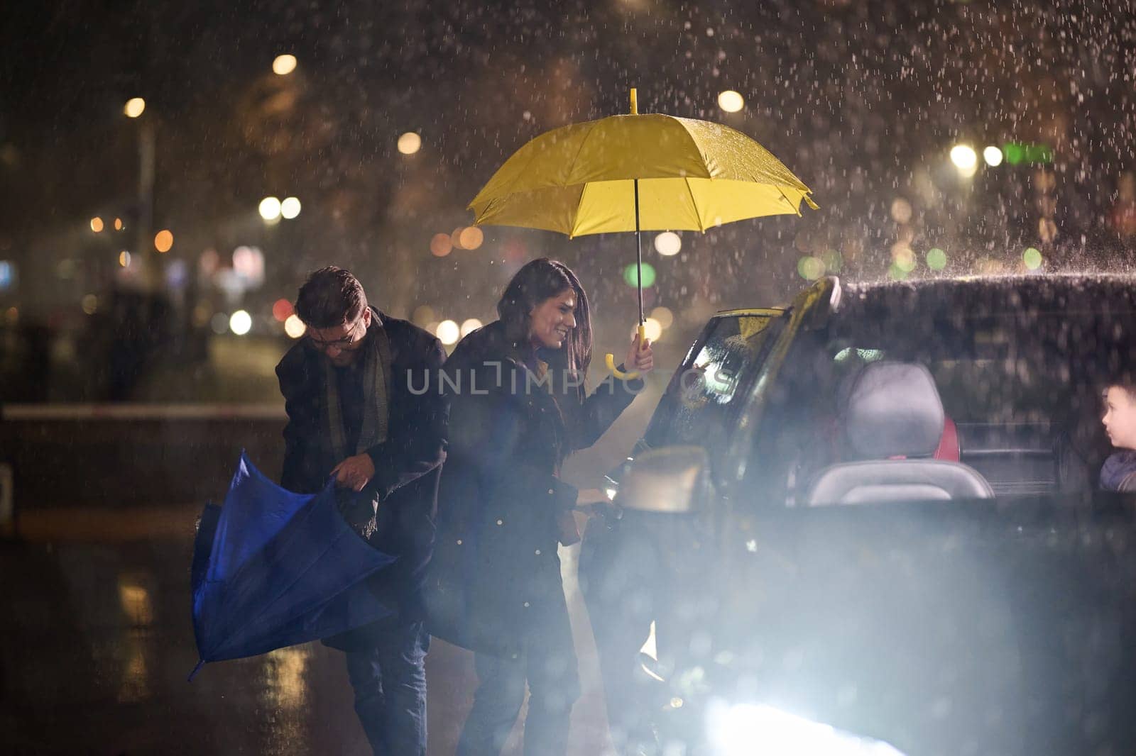 A family man lovingly opens the car for his family in rainy weather, sheltering them with an umbrella.
