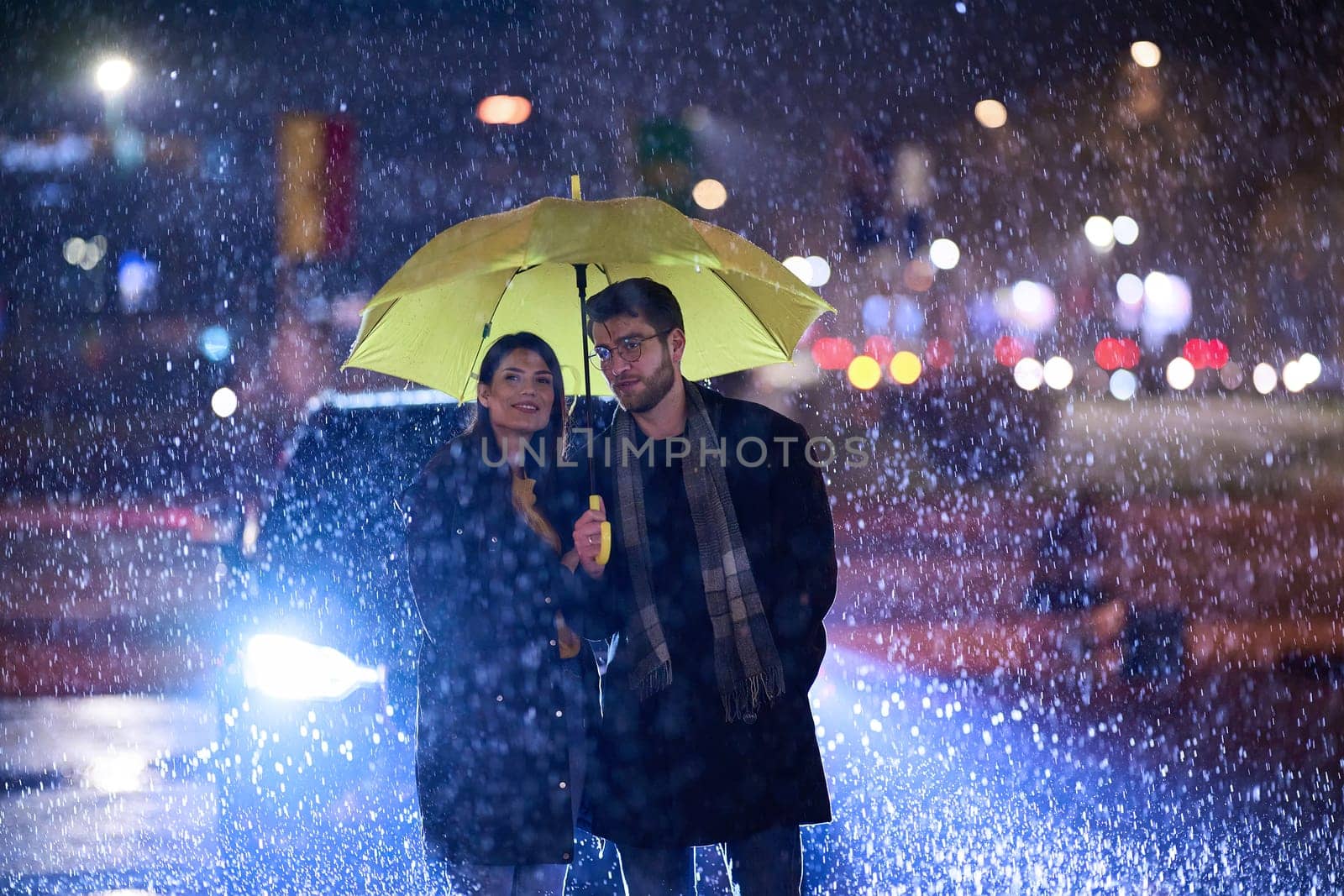 In the romantic ambiance of a rainy night, a happy couple walks through the city, sharing tender moments under a yellow umbrella, surrounded by the glistening glow of urban lights.