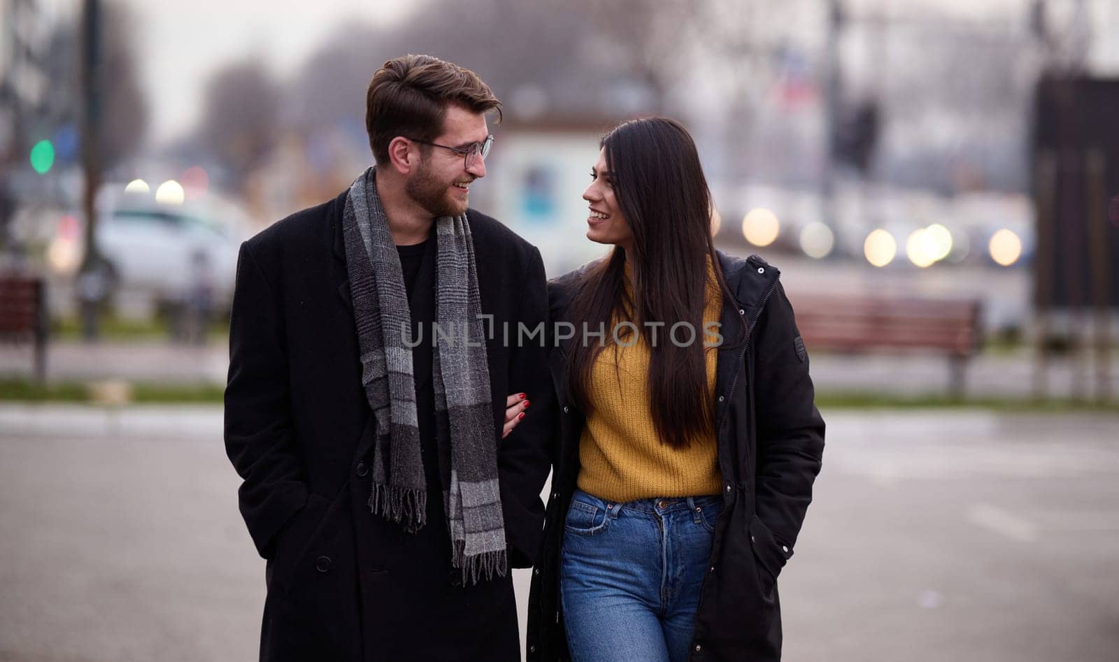 A romantic couple embraces in a tender hug as they stroll through the city streets, enjoying leisure time together in each other's company.