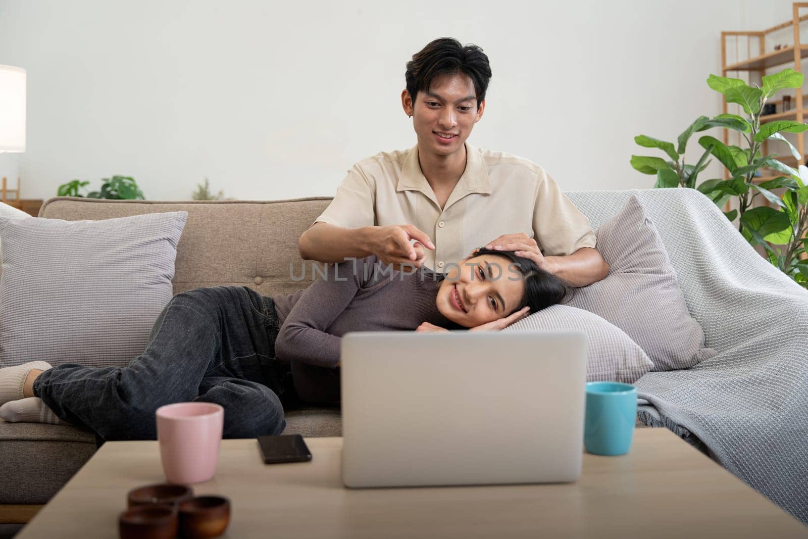 Happy couple asian sit relax on couch in living room watching video on laptop together at home.