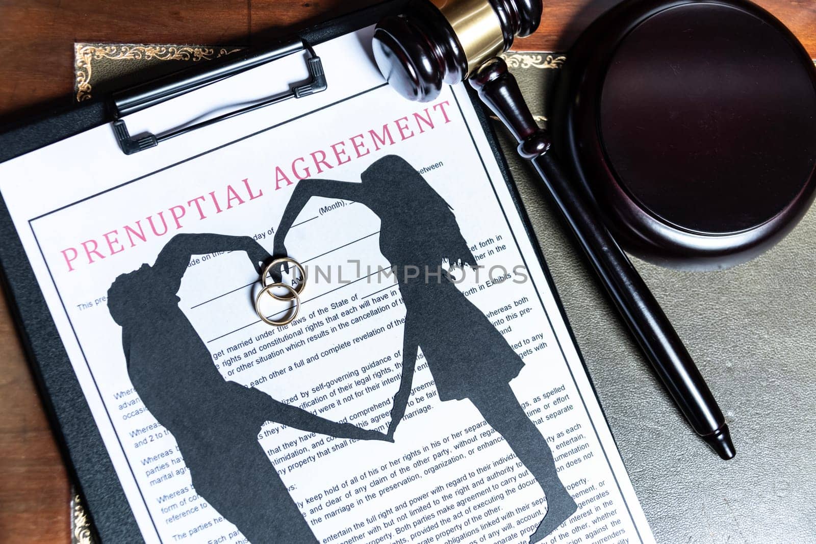 A clipboard holding a prenuptial agreement with a cut-out silhouette of a couple and wedding rings, next to a judge's gavel. by jbruiz78