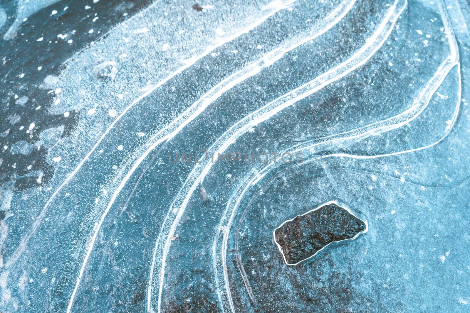 Tin cover resting on the surface of the water, with distinctive pattern of parallel white lines. In background, black rock protrudes from icy surroundings, adding texture and contrast to winter landscape. High quality photo