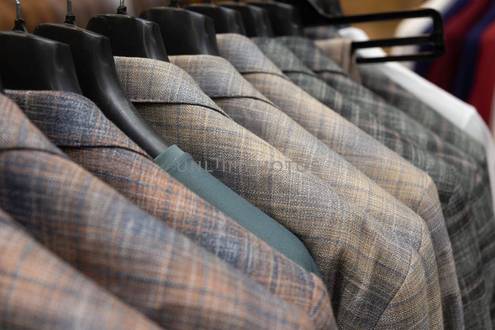 A row of men's suits, jackets hanging on a rack for display. Elegant man suit jackets hanging in a row with close up of sleeve and buttons.