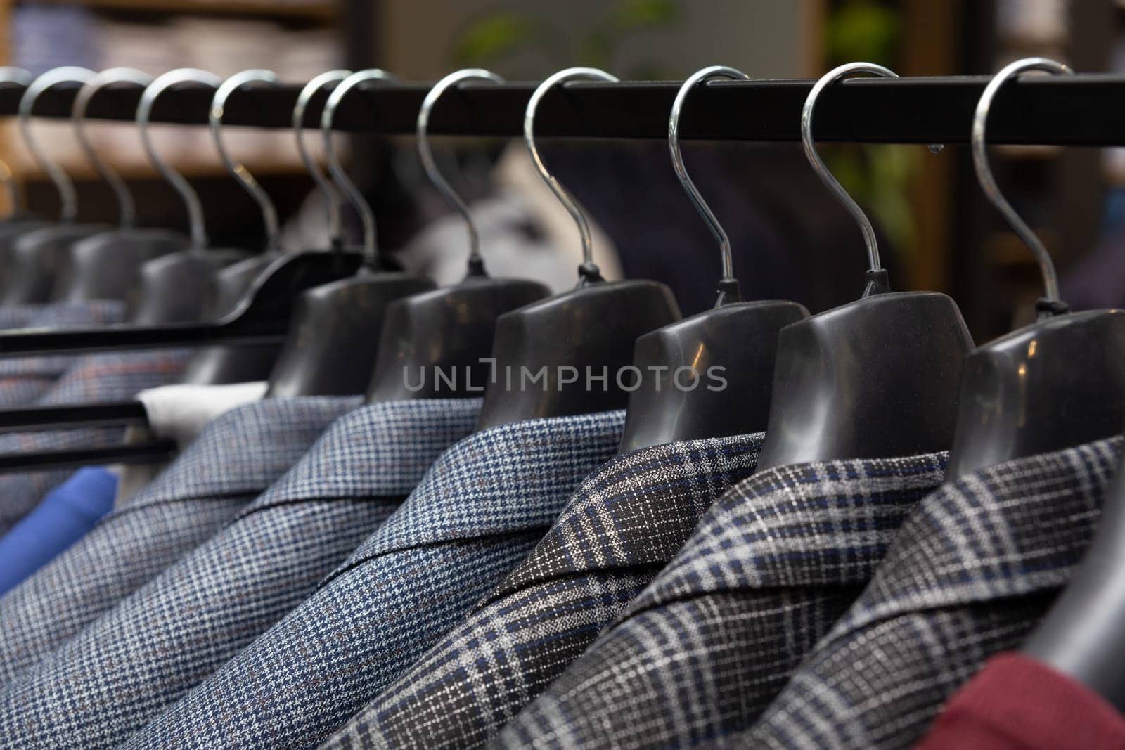 A row of men's suits, jackets hanging on a rack for display. by BY-_-BY