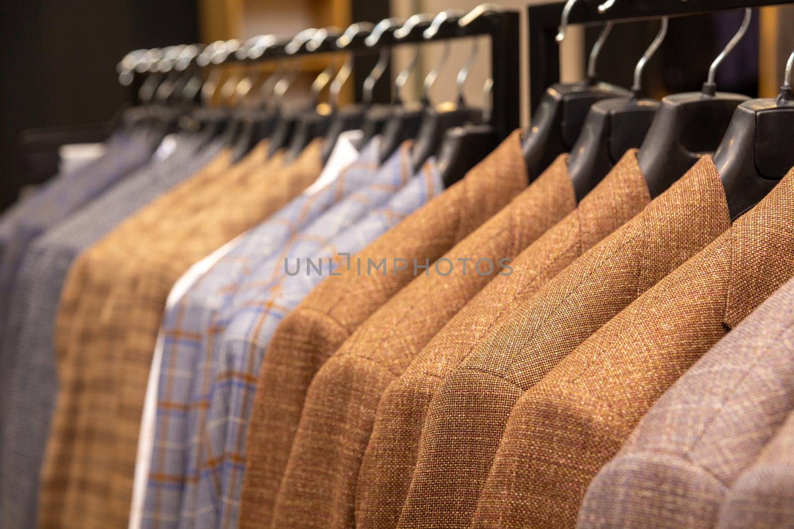 A row of men's suits, jackets hanging on a rack for display. Elegant man suit jackets hanging in a row with close up of sleeve and buttons.