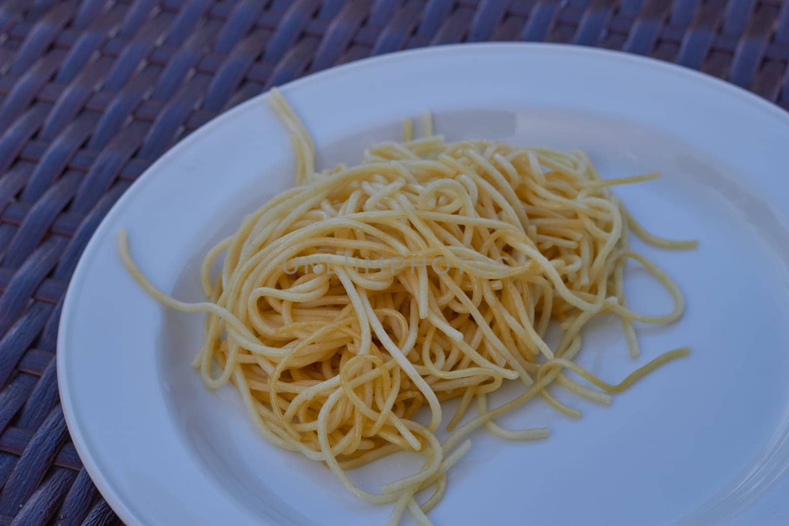 spaghetti on a white plate on a rattan table. by electrovenik