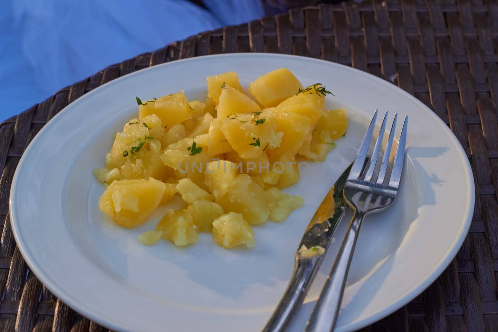 Photo fried potatoes with dill on a white plate. Metal fork and knife. Table setting. Serving lunch. Food.