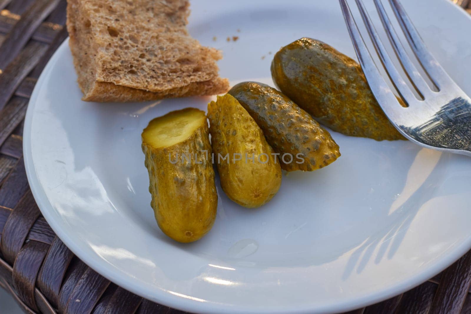 Photo pickled sliced cucumbers, a piece of rye bread on a white plate. Simple food.